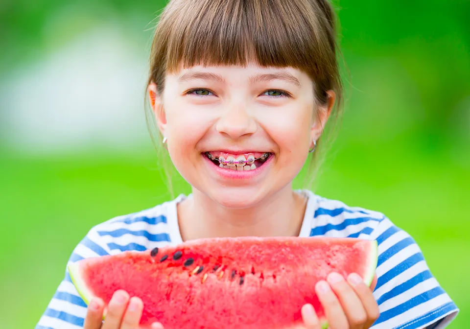 Smiling girl with braces holding a slice of watermelon